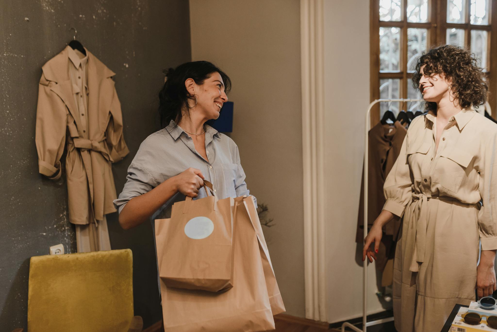 Two women enjoying a shopping experience in a boutique, smiling and carrying bags.