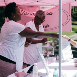 Two women selling goods to a customer at an outdoor stall during the day.