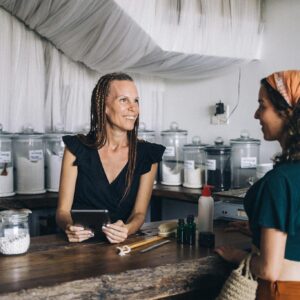 Woman using a tablet to assist customer in eco-friendly store with jars and eco products.